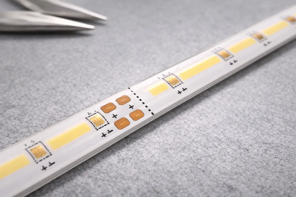 Close-up of a COB LED strip showing a cut mark (scissor icon/printed line) and adjacent copper pads that align with connectors or solder points.